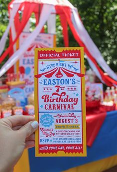 a person holding up a ticket for an amusement park birthday party with circus tents in the background