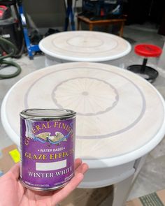 a hand holding a can of paint in front of several tables with chairs behind it