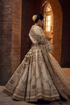 a woman in a white and gold wedding dress standing near a brick wall with her back turned to the camera