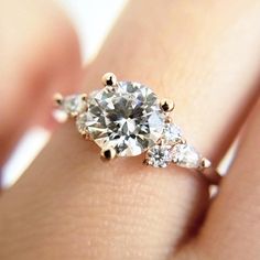 a woman's hand holding an engagement ring with three diamonds on top of it