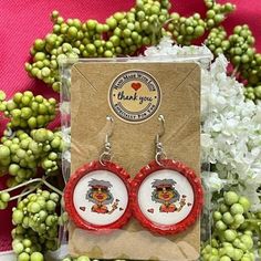 a pair of red and white earrings sitting on top of a table next to flowers