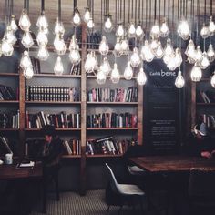 people sitting at tables in a library with bookshelves and chandeliers hanging from the ceiling