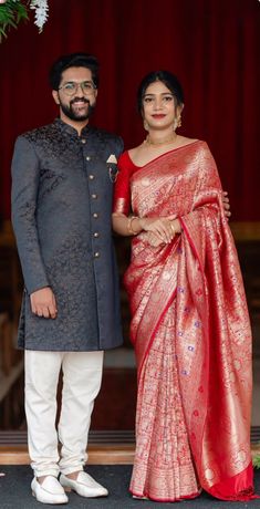 a man and woman standing next to each other in front of a red curtain with white flowers