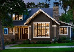 a house that is lit up at night with the lights on and trees in front