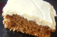 a piece of carrot cake with white frosting on a black plate, ready to be eaten