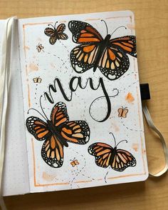 an open notebook with butterflies on it and the word may written in black ink, next to a pair of scissors