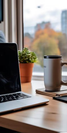 an open laptop computer sitting on top of a wooden desk next to a coffee cup