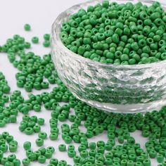 a glass bowl filled with green beads on top of a white table next to a pile of smaller green beads