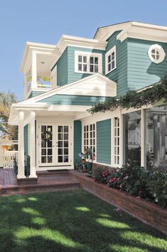 a blue house with white trim on the front and side windows, grass in front