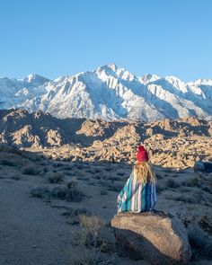 a woman sitting on top of a large rock in the middle of a desert area