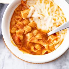 a bowl of macaroni and cheese soup with a spoon in it on a marble surface