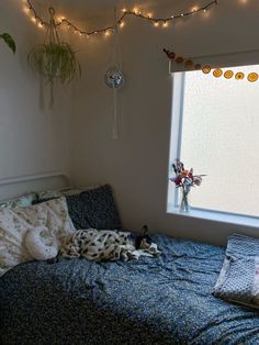 an unmade bed in front of a window with string lights