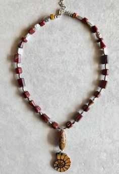 A perfect fossil Ammonite draws in the eye to a Coquina Jasper bead that dangles from earthy red Jasper beads and sterling Silver chain. Adjusts 17"-19". Jewelry 2024, Jasper Beads, Red Jasper, Sterling Silver Chain, Earth Tones, Sterling Silver Chains, Pendant Necklaces, Fossil, Silver Chain