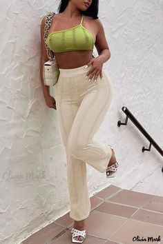 a woman leaning against a wall with her hands on her hips and wearing white pants