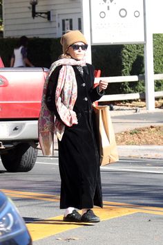 a woman walking down the street with her hand in her pocket and wearing a scarf around her neck