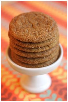 a stack of cookies sitting on top of a white cake plate in front of an orange and blue tablecloth