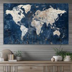 a large blue and white world map hanging on the wall above a wooden table with potted plants