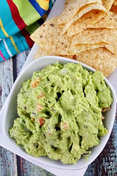 a white bowl filled with guacamole next to tortilla chips on a table