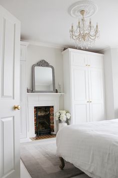 a white bedroom with a fireplace and chandelier