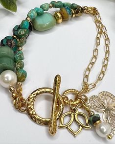 This stunning bracelet is made with beautiful high quality Turquoise Nugget Beads, Gold filled Cable Chain and more!  The asymmetrical design is so pretty with the Toggle Clasp hammered for texture and style The other beads are Heishi Aventurine, Pearls, Czech Hibiscus, Spacer Beads, & Glass Czech Beads  The Gold Alloy Butterfly Charm is lightweight and next to the Gold Plated Lotus Charm they are the perfect touch to finish off this amazing bracelet.  This bracelet is 7 inches big fits asymmetrically with the toggle in the side of the wrist. It is comfortable and would look great as an addition to your bracelet collection! It is not adjustable.  I appreciate your business and do my little happy dance with every sale!  I hope you can see my real passion and attention I give to making each Bohemian Gold Pearl Bracelet With Gemstone Beads, Gold Bohemian Pearl Bracelet With Gemstone Beads, Bohemian Turquoise Charm Bracelet With Lobster Clasp, Handmade Green Pearl Bracelet In Bohemian Style, Handmade Green Bohemian Pearl Bracelet, Handmade Green Pearl Bohemian Bracelet, Green Bohemian Metal Beaded Bracelets, Green Bohemian Metal Beaded Bracelet, Gold Alloys