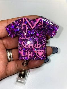 someone is holding up a purple glitter shirt keychain with the words scrub life on it