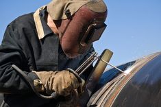 a man wearing a gas mask grinding metal on a piece of equipment in his hands