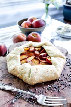 an apple pie on a cutting board with a fork and bowl of fruit in the background