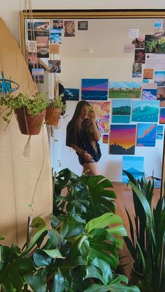 a woman standing in front of a wall with plants on it and pictures behind her