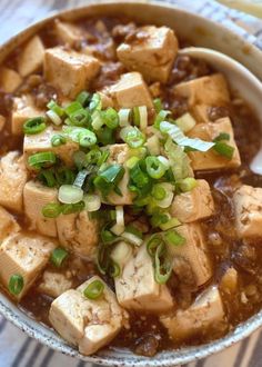 a bowl filled with tofu and green onions on top of a striped table cloth