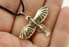 a hand holding a small gold pendant with a bird on it's back and wings