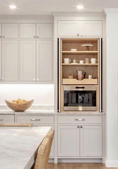 a kitchen with white cabinets and an oven in the center, along with a bowl of fruit on the counter