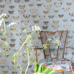 a chair sitting in front of a wall with butterflies on it and a plant next to it