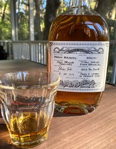 a bottle of whiskey sitting on top of a wooden table next to a glass cup