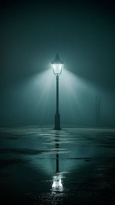 a lamp post in the middle of an empty parking lot at night with light shining on it