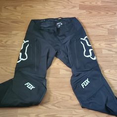 a pair of black pants with white fox logos on them sitting on a wooden floor