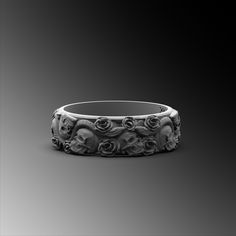 an intricately designed wedding ring with skulls and roses on it's side, against a black background