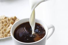 a person pouring milk into a cup of coffee with waffles on the side