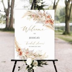 a welcome sign with flowers and greenery is displayed on an easel in front of trees