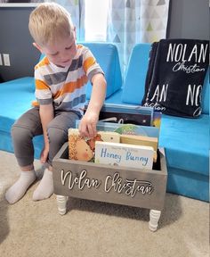 a young boy sitting on top of a blue couch next to a wooden box filled with books