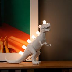 a light up dinosaur figure sitting on top of a wooden table next to a painting