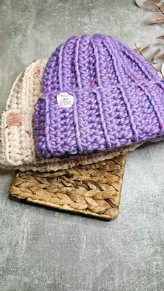 two knitted hats sitting next to each other on top of a woven piece of wood