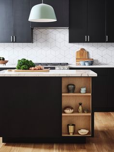 a kitchen with black cabinets and white tile backsplash, an island in the middle