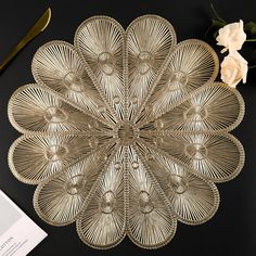 an intricately designed metal plate next to a flower and knife on a black surface