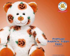 a white and orange teddy bear with pumpkins on it's face, sitting in front of an orange background