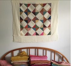 a pile of folded clothes sitting on top of a bed next to a wall hanging