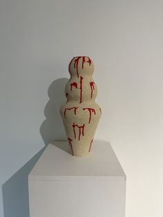 a white and red vase sitting on top of a pedestal in front of a wall