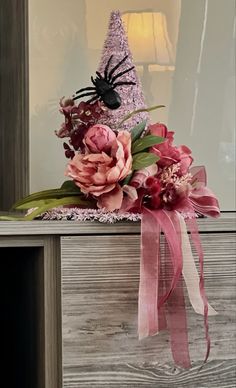 a vase filled with flowers and a spider on top of a wooden table next to a lamp