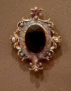 a gold brooch with a black stone in the center on a tan surface,