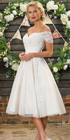 a woman in a short white dress standing next to a wall with flowers on it