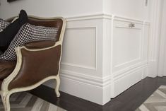 a brown leather chair sitting next to a white wall with black and white pillows on it